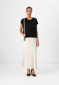 Top nero drappeggiato con maniche corte, abbinato a una lunga gonna color crema. Indossato con scarpe nere con tacco alto e una piccola borsa bianca.
