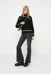 Melnā džemperis ar baltajiem akcentiem, apvienots ar pelēkiem flared džinsiem un masīviem melniem platformas zābakiem. Vienkāršs dizains ar ikdienišķu piegulšanu.