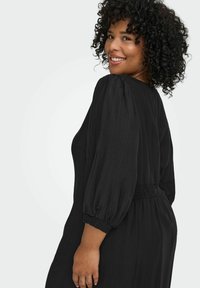 Melna kleita ar pūkainām piedurknēm, elastīgu jostasvietu, teksturētu audumu. Dizainā ir atsvaidzinoša piegriezuma un gluda apdare.