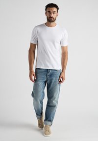Vit t-shirt med kort ärm, i bomull, crew neckline, kombinerad med ljusblå avslappnade jeans och beige sneakers. Minimalistisk design.