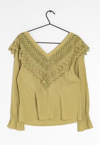 Blusa verde oliva con ampio scollo a V, caratterizzata da intricate decorazioni in pizzo sulle spalle e sui polsini, tessuto fluido con finitura testurizzata.