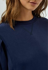 Sudadera azul marino con cuello redondo, que presenta un pespunte texturizado en el escote. La tela parece suave y lisa.