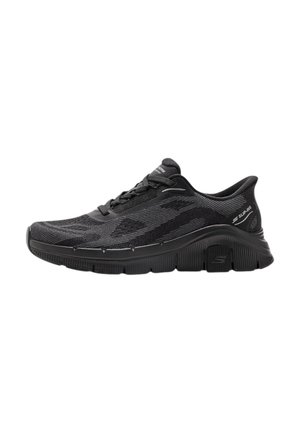 Sneaker sportiva nera con tomaia in maglia testurizzata, chiusura con lacci, suola spessa imbottita e design antiscivolo, vista laterale su sfondo bianco.