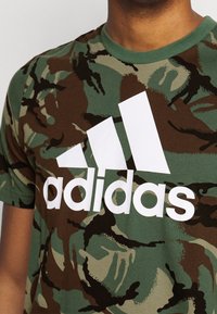 Groene camouflage t-shirt met een wit Adidas-logo. Ronde hals, korte mouwen, gemaakt van zachte katoenmix met een gladde textuur.