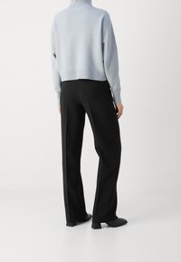 Lichtblauwe cropped coltrui met geribde manchetten, gecombineerd met hoge zwarte wijde broek en zwarte enkellaarsjes.