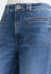 Jeans in denim blu con un design classico, caratterizzati da vita alta, tasche frontali e cuciture a contrasto. Il tessuto ha una superficie liscia.