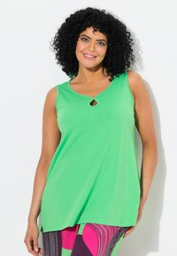 Top verde senza maniche con un dettaglio a chiave all' scollatura, realizzato in tessuto morbido. La parte inferiore ha un orlo leggermente più lungo, che completa dei pantaloni fantasia.