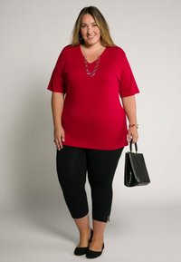 Top rosso a maniche corte con scollo a V, abbinato a leggings cropped neri e una borsa nera con texture. Ballerine nere completano l'outfit.