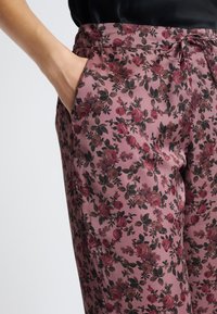 Różowe spodnie w kwiatowy wzór o satynowym wykończeniu, z regulowanym paskiem w talii i bocznymi kieszeniami, z ciemnozielonymi i burgundowymi kwiatami.