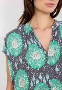Blusa grigia con motivo floreale in tonalità di verde e blu chiaro. Maniche corte, scollatura a v e leggere arricciature sulle spalle.