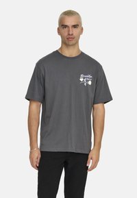 Grå bomulds t-shirt med korte ærmer, rund hals, prydet med et hvidt blomster- og tekstdesign på venstre brystområde.