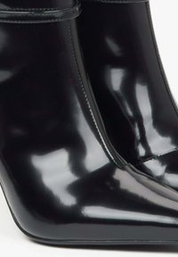 Černé lakované kotníkové boty s špičatou špičkou a štíhlým podpatkem. Mají hladký, lesklý povrch a minimální švy.