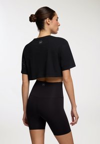Czarna krótka koszulka z miękkiego materiału z krótkimi rękawami, w połączeniu z wysokimi czarnymi szortami. Oba elementy zawierają detale z logo marki.