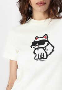 Hvit bomull t-skjorte med et tegneseriekatte-design med svart kontur, røde detaljer og teksten "KARL LAGERFELD" under grafikken.