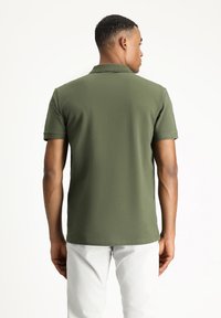 Zielona koszulka polo z krótkim rękawem, teksturowany materiał i klasyczny kołnierzyk. Widok z tyłu, z prostym obszyciem i luźnym krojem.