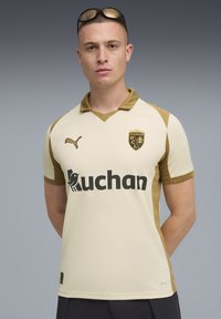 Cremfarbener Fußballtrikots mit goldenen Akzenten, ausgestattet mit einem V-Ausschnitt, kurzen Ärmeln und Logos: Puma und Ruchan. Das Material wirkt glatt und atmungsaktiv.