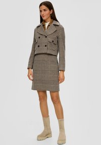 Zszywana, w kratę, kurtka z podwójnymi guzikami, w zestawie ze dopasowaną spódnicą. Beżowe zamszowe botki na grubej podeszwie dopełniają całość.
