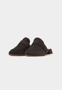 Paire de mules marron foncé à enfiler avec un petit talon bloc et une large bride sur le dessus sur un fond clair uni.