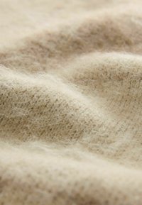 Blød beige uldstof med en fuzzy tekstur og synlig strikmønster, der viser bløde folder og naturlige fibre.
