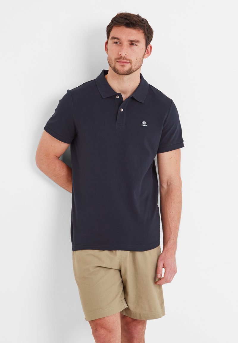 Navy polo shirt made of cotton with a classic collar, short sleeves, and a small logo on the chest, paired with beige shorts.