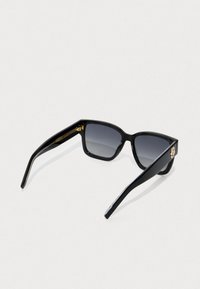 Μαύρα ορθογώνια γυαλιά ηλίου με σκούρες γκριδατές φακούς και χρυσά λογότυπα στα μπράτσα, τοποθετημένα σε ανοιχτό φόντο.