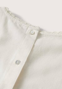 Tissu blanc avec deux petits boutons blancs et une délicate bordure en dentelle le long d'un col arrondi.