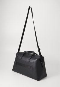 Sac de sport noir en matériau texturé, doté de poignées doubles, d'une bandoulière réglable et d'un panneau solide sur le devant.