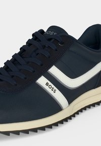 Baskets bleu marine avec bandes blanches et marquage "BOSS", design à lacets et semelle extérieure noire rainurée sur fond clair.