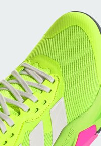 Neon žalios spalvos sportiniai batai su tekstūruota tinklinė viršutine dalimi, baltais akcentais ir rožine guminėmis padais. Yra reguliuojama raištelių sistema, užtikrinanti tvirtą prigludimą.