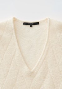 Cremefarbener, flauschiger Strickpullover mit V-Ausschnitt und einem schwarzen Etikett mit der Aufschrift "someday." und der Größe "36" am Hals.