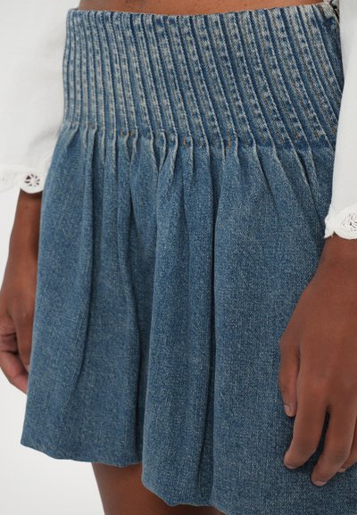 Falda de mezclilla con cintura fruncida, diseño plisado y un lavado azul medio. Superficie texturizada con un ligero desgaste y sin patrones visibles.