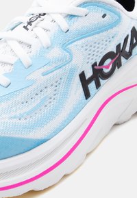 Ανοιχτό μπλε και λευκό παπούτσι για τρέξιμο με λευκά κορδόνια, μαύρο λογότυπο "HOKA" και ροζ ρίγα διακόσμησης στη λευκή σόλα.