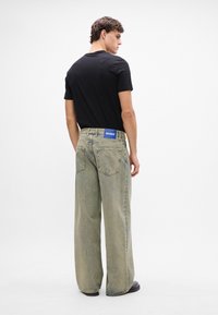 Világoskék, laza fazonú farmernadrág, mely denim anyagból készült, hátsó derékrészen márkázott kék címkével és két hátsó zsebbel rendelkezik.