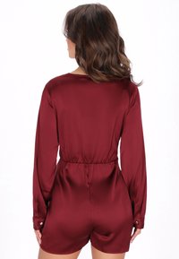 Burgundský saténový overal s dlouhými rukávy, elastickým pasem a knoflíkovými manžetami. Hladká textura s přiléhavým střihem a délkou šortek.