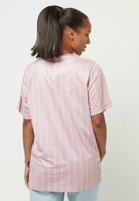 Helles rosa Kurzarmhemd mit vertikalen weißen Streifen, rundem Ausschnitt und entspannter Passform. Verfügt über ein dezentes Logo an der Seite.
