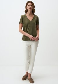 T-shirt verde oliva a maniche corte con scollatura a V, abbinato a pantaloni bianchi aderenti e mocassini in camoscio marrone. Texture liscia, stile casual.