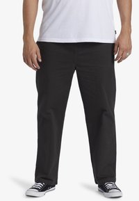 Pantaloni di cotone neri con vestibilità dritta, cuciture in vista e tasche frontali. Abbinati a sneaker in canvas nere e una t-shirt bianca.