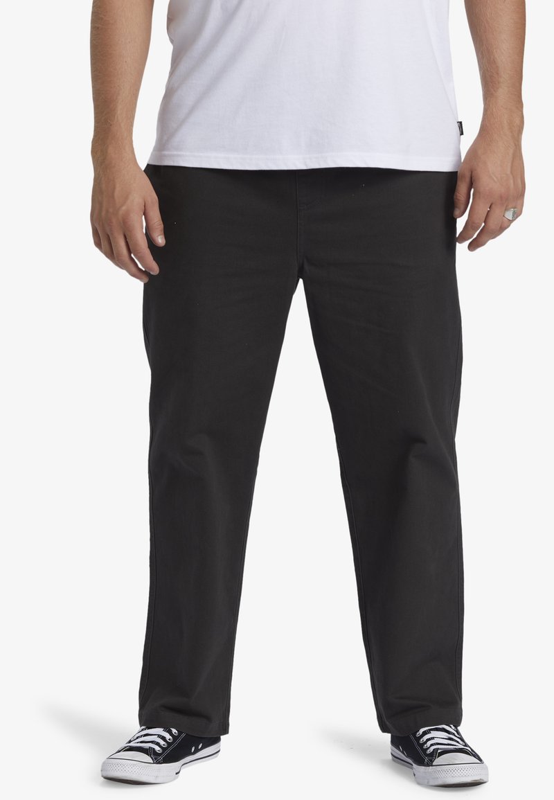 Pantaloni di cotone neri con vestibilità dritta, cuciture in vista e tasche frontali. Abbinati a sneaker in canvas nere e una t-shirt bianca.