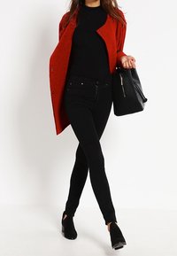 Punainen villatakki, musta slim-fit paita ja mustat pillifarkut. Mustat nilkkurit ja teksturoitu musta käsilaukku täydentävät asun.