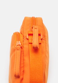 Oransje polstret veske med to glidelås lukkinger. Laget av teksturert nylon, har matchende stoff glidelåshåndtak og vevde stroppdetaljer.