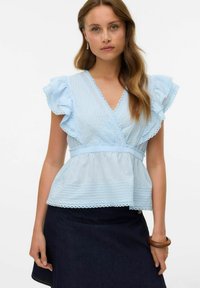 Haut peplum bleu clair avec des manches volantes, des rayures verticales texturées et un ourlet festonné. Porté avec une jupe en denim foncé.