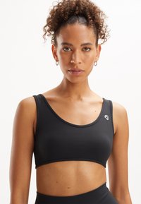 Bra sportivo nero realizzato in tessuto liscio, con scollatura rotonda, spalline larghe e un piccolo logo sul lato sinistro.