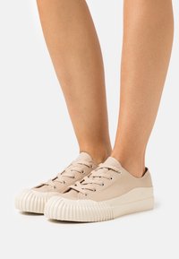 Beige canvas sneakers med rundade, räfflade gummisulor och fem snörningsöglor. Minimalistisk design med en slät yta och lätt konstruktion.