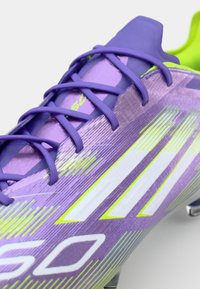 Purple soccer cleat featuring textured upper with light green accents, elongated stripes, and flat laces. Reinforced toe cap and sleek design.