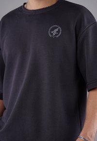 Schwarzes Baumwoll-T-Shirt mit rundem Halsausschnitt, kurzen Ärmeln und einem leicht ausgewaschenen, strukturierten Finish. Mit einem kleinen Logo-Print in Weiß.