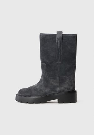Botte mi-mollet en daim noir avec languette d'extraction, bout rond et semelle épaisse en caoutchouc noir, vue de côté gauche sur fond uni.