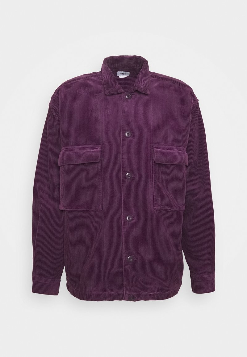 Lila kordflöjelskjorta med knappar och krage, samt två stora framfickor, uppvisad mot en vit bakgrund.