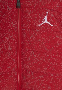 Rode puffervest met een ritssluiting aan de voorkant, voorzien van een textuurpatroon in lichter rood en een witte Jumpman-logo op de borst.