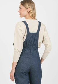 Dżinsowy kombinezon z regulowanymi ramiączkami, tkanym pasem w talii i luźnym krojem. Wewnętrznie wyłożony lekkim, prążkowanym beżowym topem.