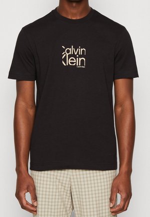 T-shirt en coton noir avec un logo Calvin Klein beige au centre. Il a des manches courtes et un col rond avec un ourlet droit.